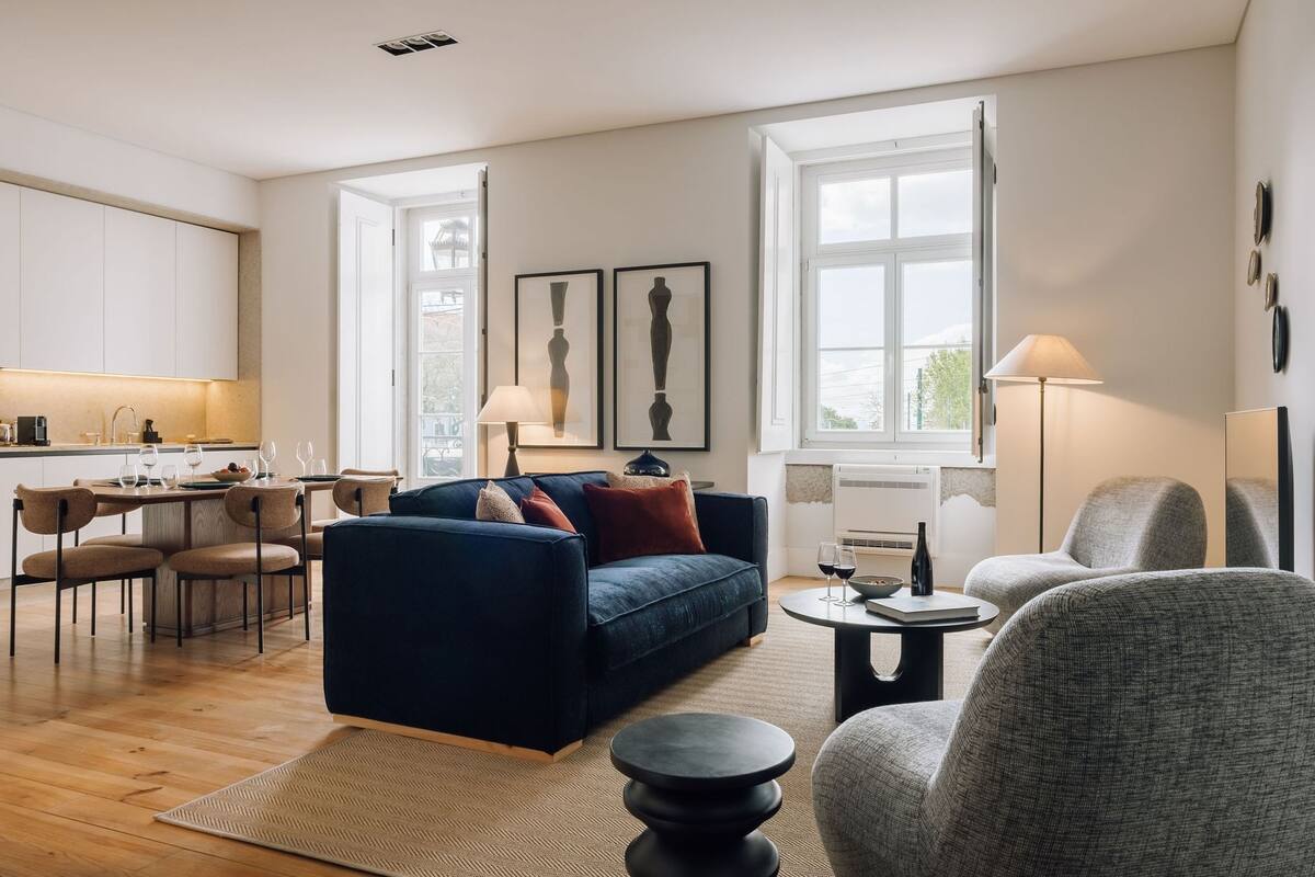Ein modernes Wohnzimmer mit einem dunkelblauen Sofa, einem grauen Sessel und einem Essbereich mit einem Holztisch und Stühlen.