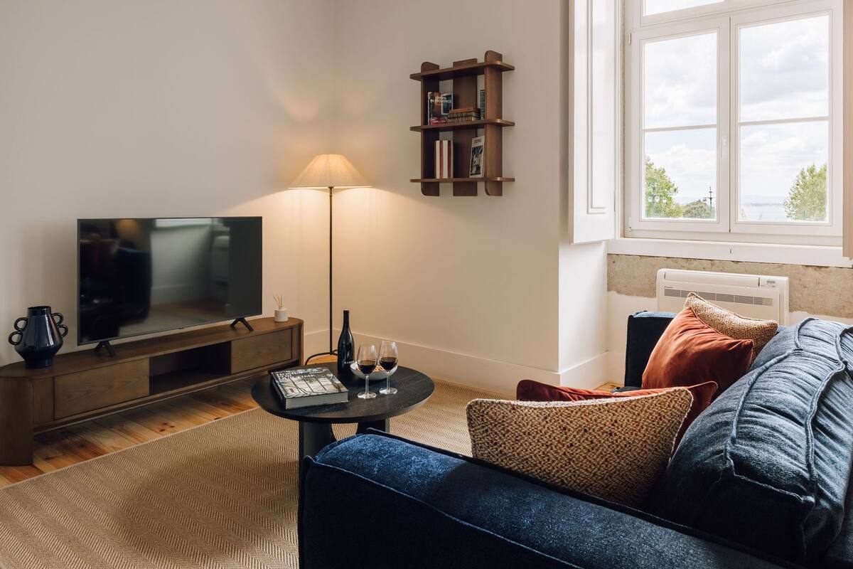 Ein Wohnzimmer mit Fernseher, Lampe, Bücherregal und einem Fenster mit Blick.