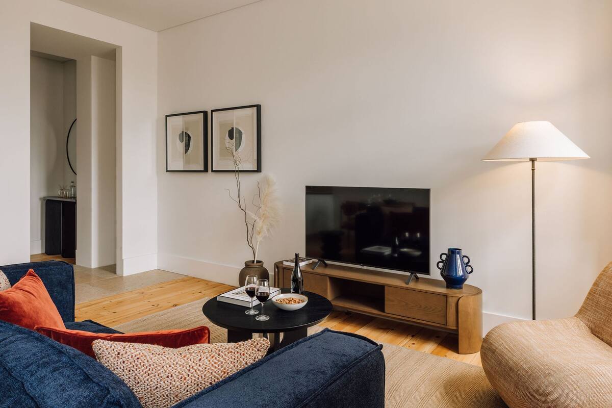 Ein modernes Wohnzimmer mit einem Flachbildfernseher, einem Couchtisch mit einer Schüssel Frühstücksflocken und Weingläsern sowie einer Lampe.