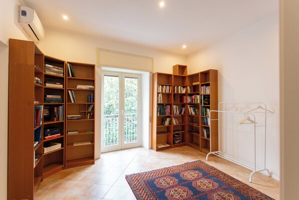 A spacious room with a large bookshelf, a door leading to a balcony, and a clothing rack.