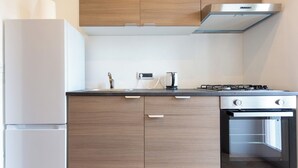 A modern kitchen with wooden cabinets, a stainless steel refrigerator, a gas stove, and a built-in oven. - Vico Santa Maria del Pozzo 9 (Naples)