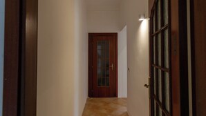 A narrow hallway with a wooden door at the end, a light fixture on the wall, and a tiled floor. - Vico Santa Maria del Pozzo 9 (Naples)