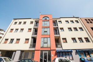 Un immeuble à plusieurs étages, doté de balcons, d’une entrée principale et de locaux commerciaux au rez-de-chaussée.