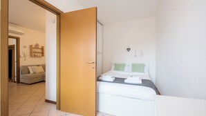 A hotel room with a bed, a bedside table, a wardrobe, and a sofa in the adjacent living area.