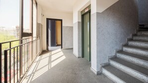 A corridor with a staircase, a balcony with a metal railing, and a door with a sign.