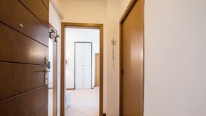 A hallway with a wooden door on the left, a white door at the end, and a wall-mounted light fixture.