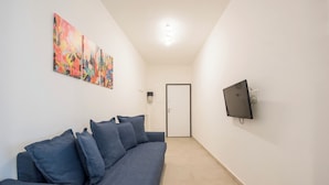Una sala de estar moderna con un sofá gris, un televisor de pantalla plana montado en la pared y un cuadro abstracto colorido sobre el sofá.