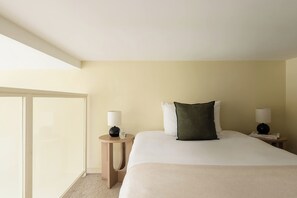 A hotel room with a large bed, two bedside tables with lamps, a window, and a view of the outside.