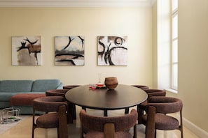 A dining area with a round table surrounded by eight chairs, a vase, and two glasses on the table.
