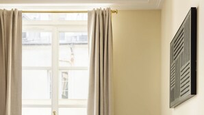 Una habitación de hotel con cama, mesita de noche, lámpara y ventana con cortinas.