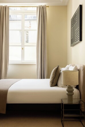 A hotel room with a bed, a bedside table, a lamp, and a window with curtains.