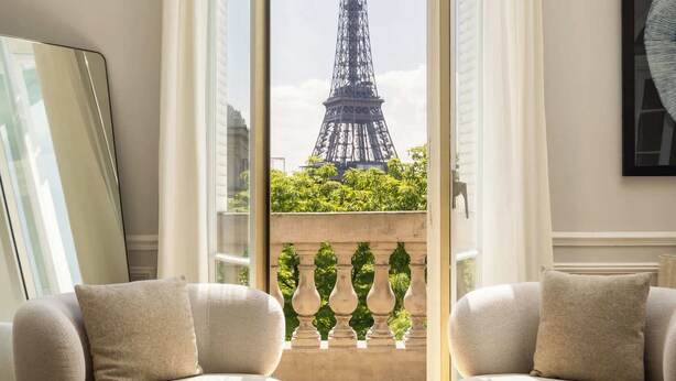 Una habitación con vista a la Torre Eiffel, una mesa redonda con un libro y un cuenco, dos sofás y un espejo grande.