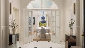 Un umbral abierto que da a un comedor con vistas a la Torre Eiffel, suelo de baldosas blancas y una mesa de cristal con sillas.
