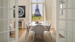Un comedor con vista a la Torre Eiffel a través de una ventana, una mesa blanca con sillas y un espejo decorativo.