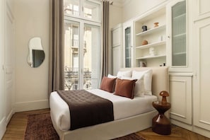 Een slaapkamer met een bed, nachtkastje en een raam met uitzicht op een balkon.