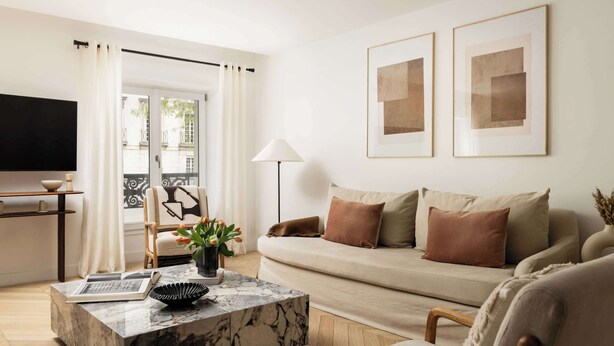 A modern living room with a sofa, a coffee table, a TV, and a balcony with curtains.