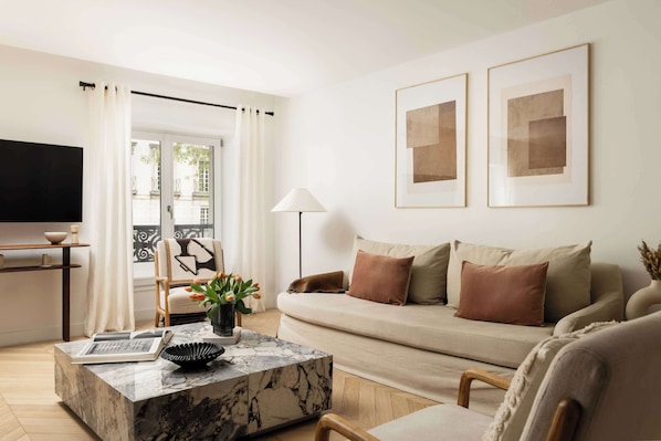 Un salon moderne avec un canapé, une table basse, un téléviseur et un balcon agrémenté de rideaux.