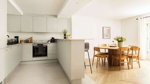 A modern kitchen with white cabinets, a built-in oven, and a dining area with wooden chairs and a table.