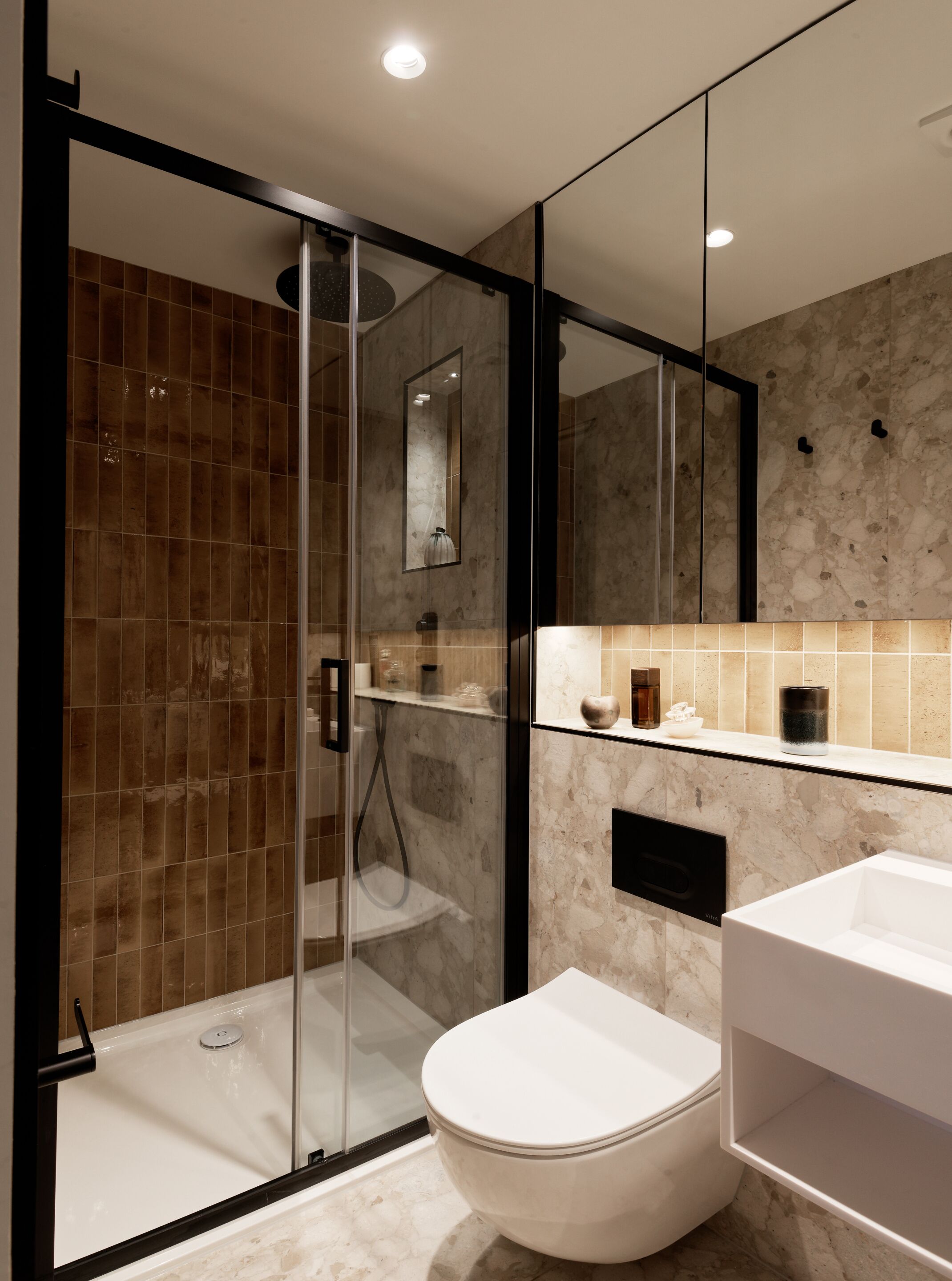 A modern bathroom with a glass-enclosed shower, a white toilet, and a marble-tiled vanity.