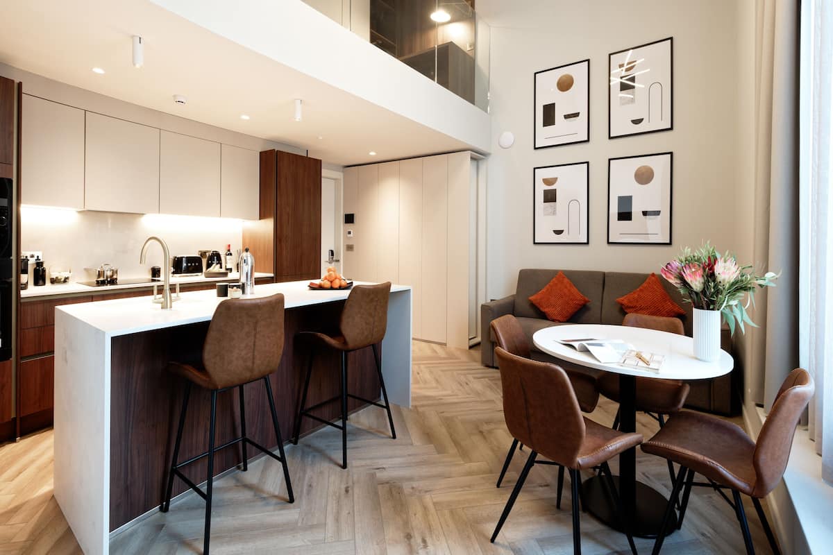 Une cuisine moderne dotée d’un îlot central, de tabourets de bar et d’une table à manger avec des chaises. Des œuvres d’art encadrées ornent le mur, et un vase rempli de fleurs est posé sur la table à manger.