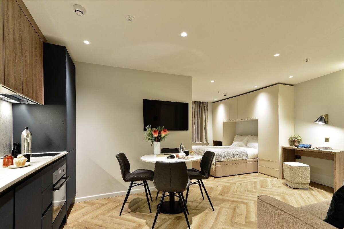 Une chambre d’hôtel moderne équipée d’une kitchenette, d’un coin repas, d’un lit et d’un bureau avec une lampe.