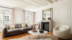 Ein Wohnzimmer mit einer Couch, Sesseln, einem Couchtisch, einem Kamin und großen Fenstern.
