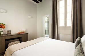 Un dormitorio con cama, un escritorio, un jarrón con flores y una ventana con cortinas.