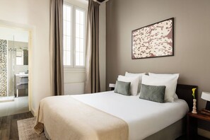 A hotel room with a bed, a bedside table with a lamp, a framed artwork on the wall, and a bathroom visible through an open door.