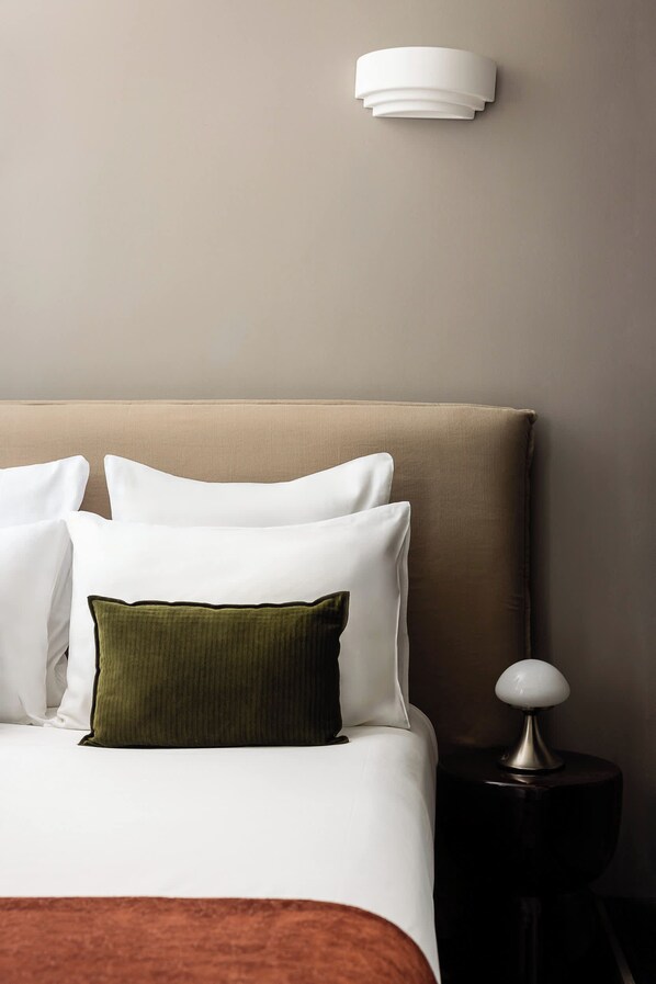 Una cama bien hecha con almohadas blancas y verdes, un cabecero marrón y una lámpara de noche sobre una mesita de noche oscura.