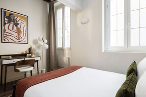 Habitación de hotel con cama, escritorio, silla, un cuadro en la pared y ventana.