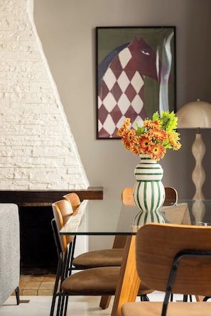 A dining area with a glass table, striped vase with flowers, and a painting on the wall.