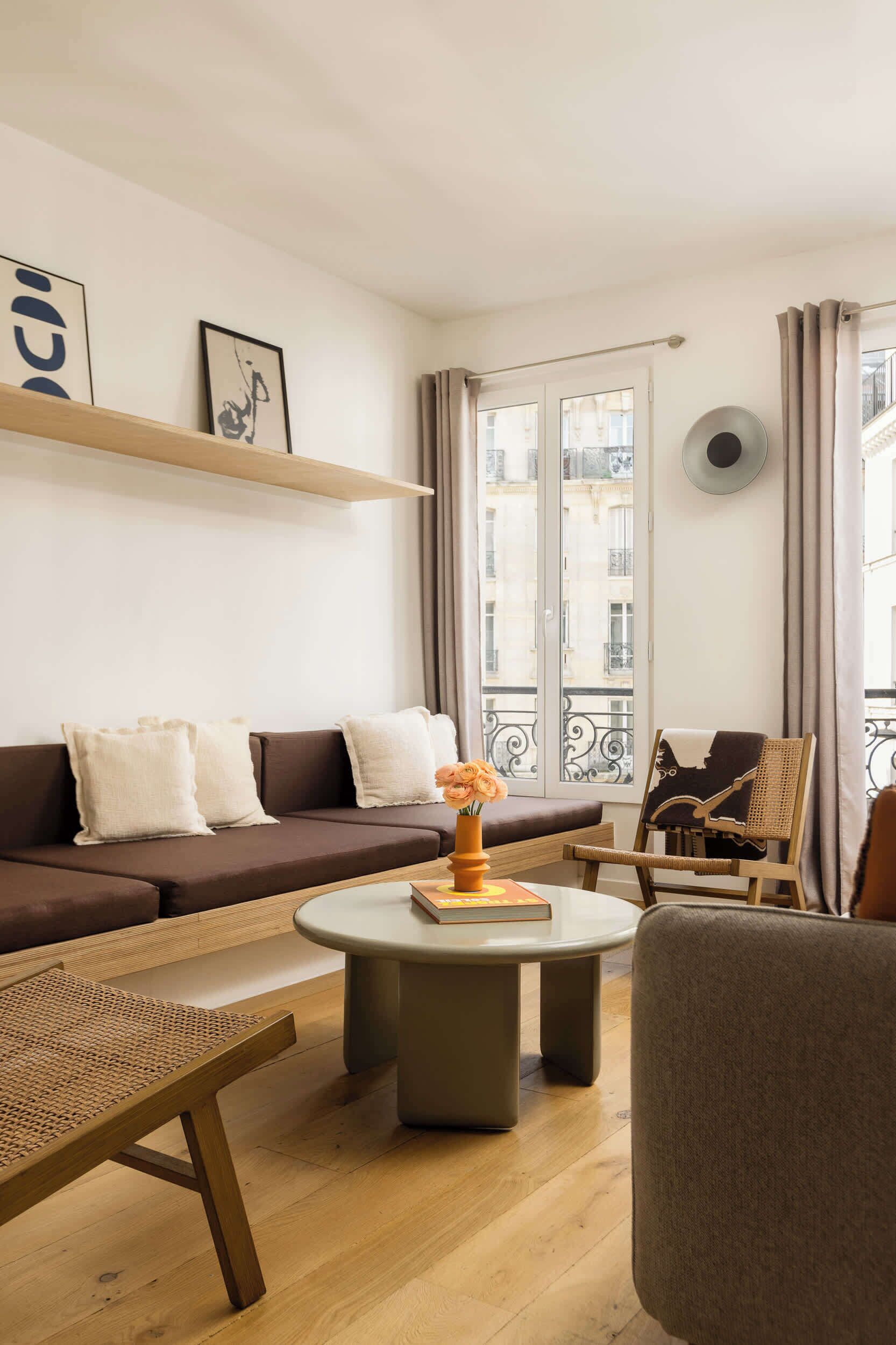 Uma sala de estar moderna com um sofá, uma mesa de centro redonda, uma poltrona de vime e vista da cidade através de grandes janelas.