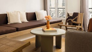 Una sala de estar moderna con un sofá, una mesa redonda de centro, una silla de mimbre y vistas de la ciudad a través de amplias ventanas.