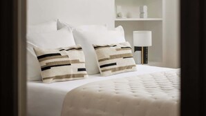 Un dormitorio con cama, almohadas, mesita de noche, lámpara, espejo y estantería.
