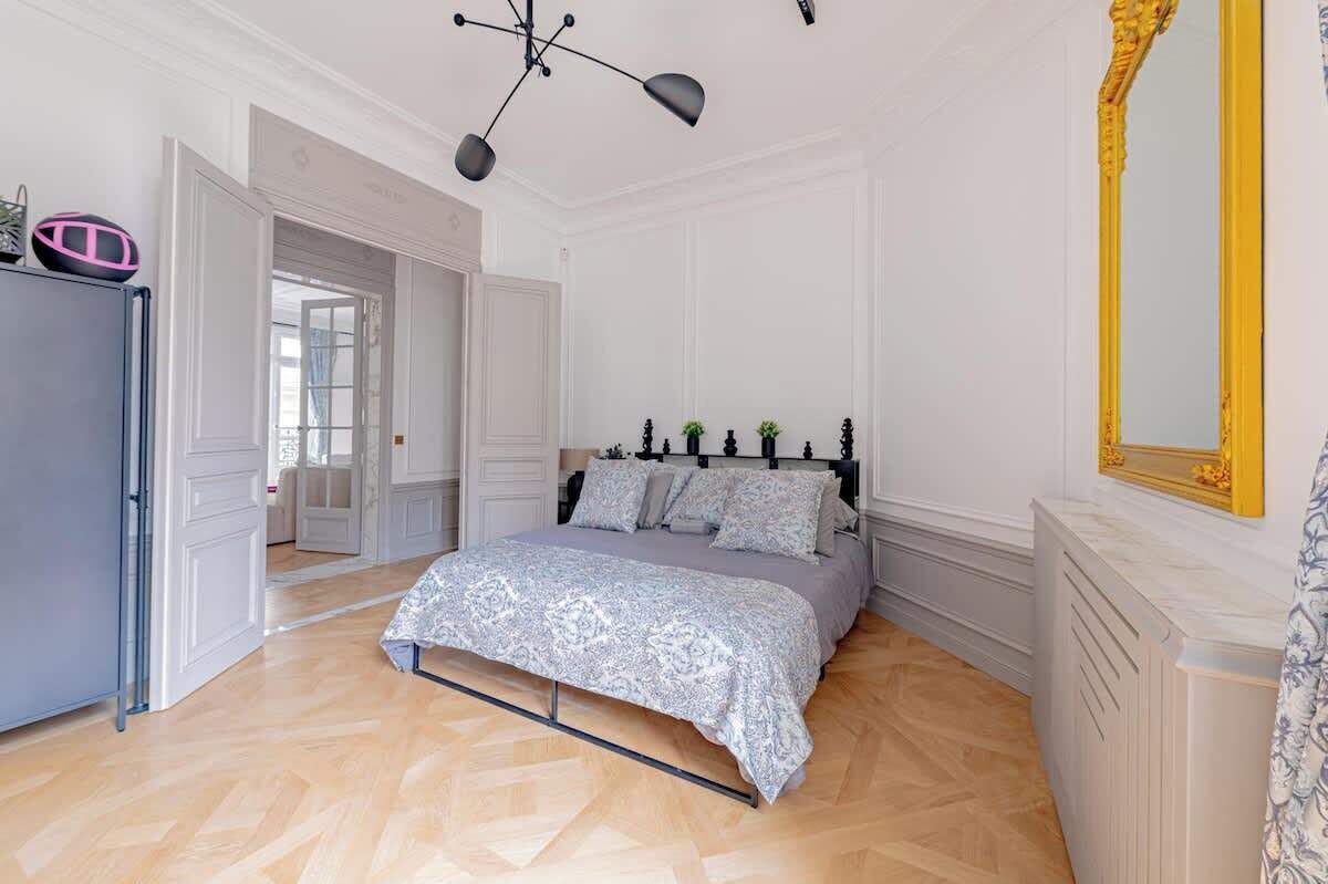 A bedroom with a bed, a wardrobe, a mirror, and a door leading to another room.