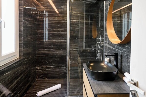 Un baño moderno con cabina de ducha de vidrio, un lavabo negro y un espejo grande.