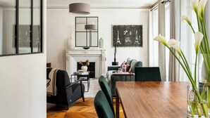 A dining area with a wooden table, green chairs, a fireplace, and a large window with curtains.