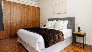 A bedroom with a bed, a nightstand, a wooden wardrobe, and a framed picture on the wall.