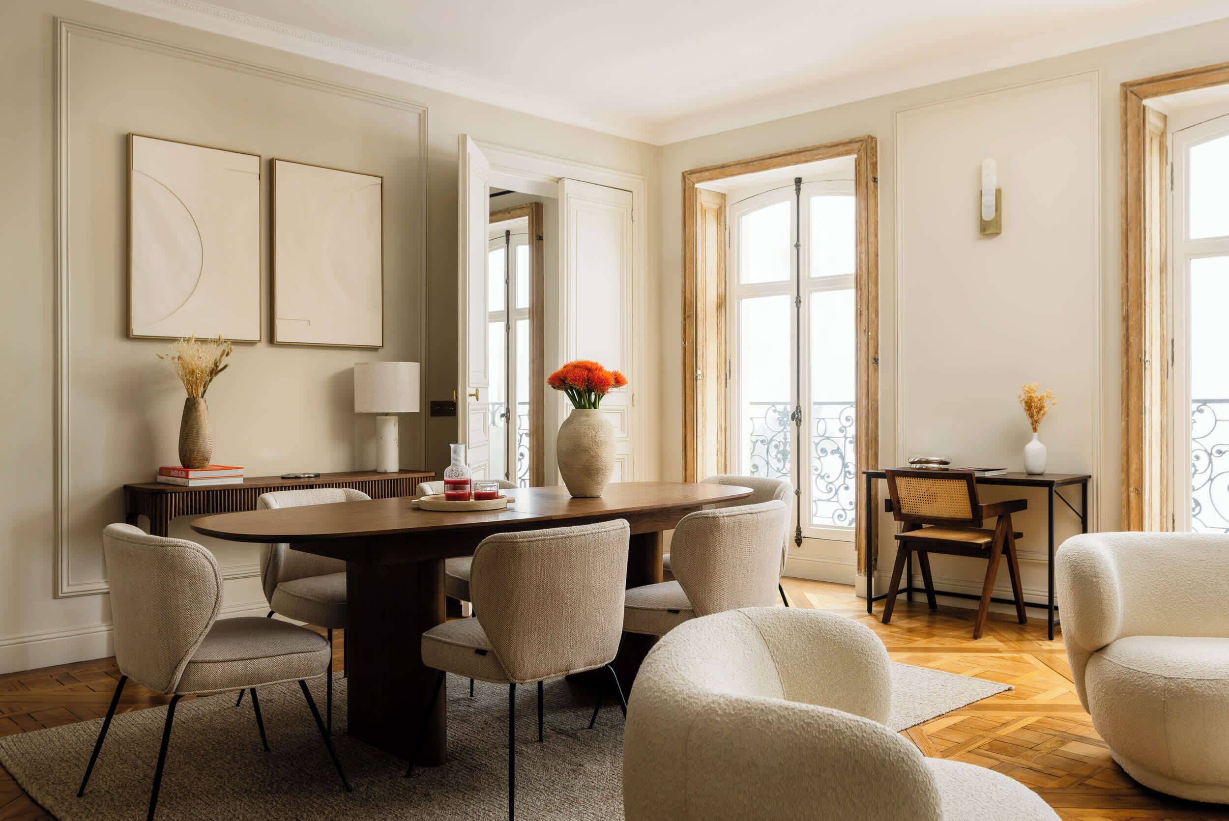A dining area with a round table, chairs, a vase with flowers, and a view of the outside.