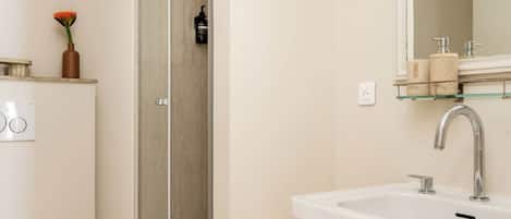 A modern bathroom with a white sink, a glass shower enclosure, and a toilet.