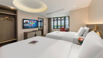Ein Hotelzimmer mit zwei Betten, einem Fernseher, einem Schreibtisch und einem Fenster mit Buntglas.