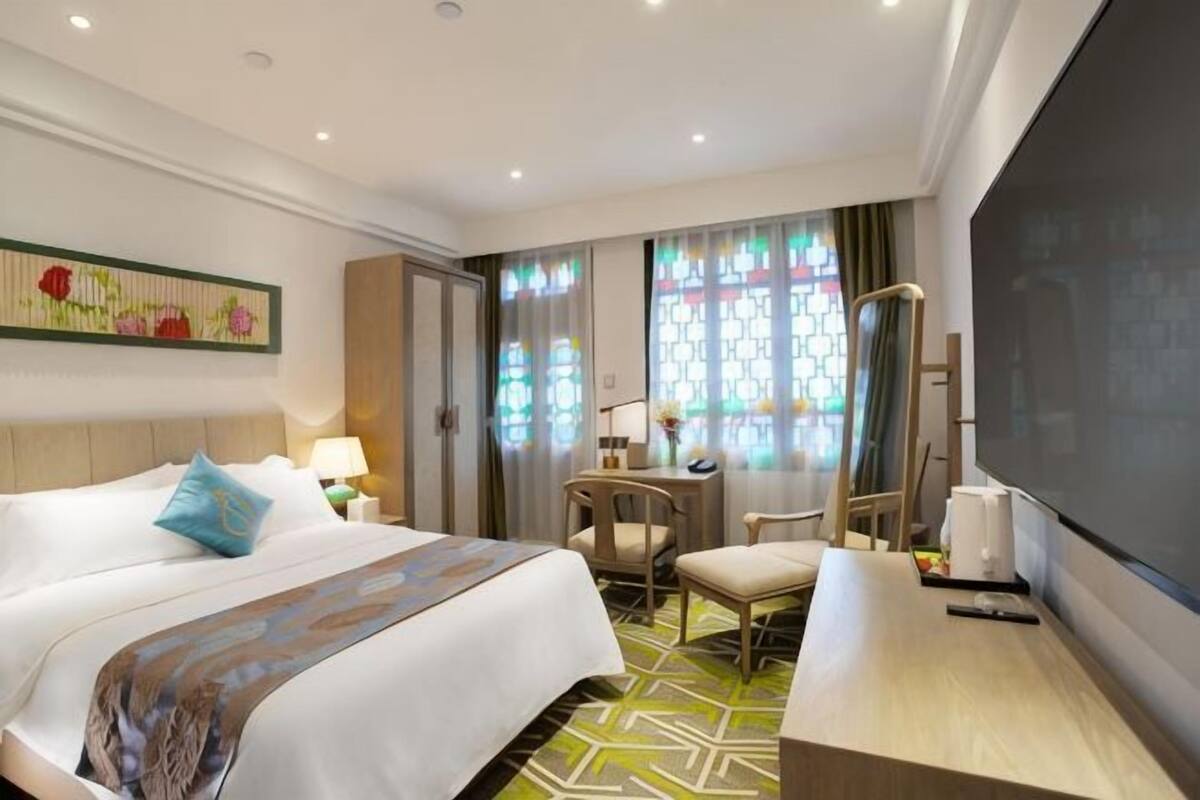 Een hotelkamer met een bed, een bureau, een stoel, een televisie en een raam met gordijnen.