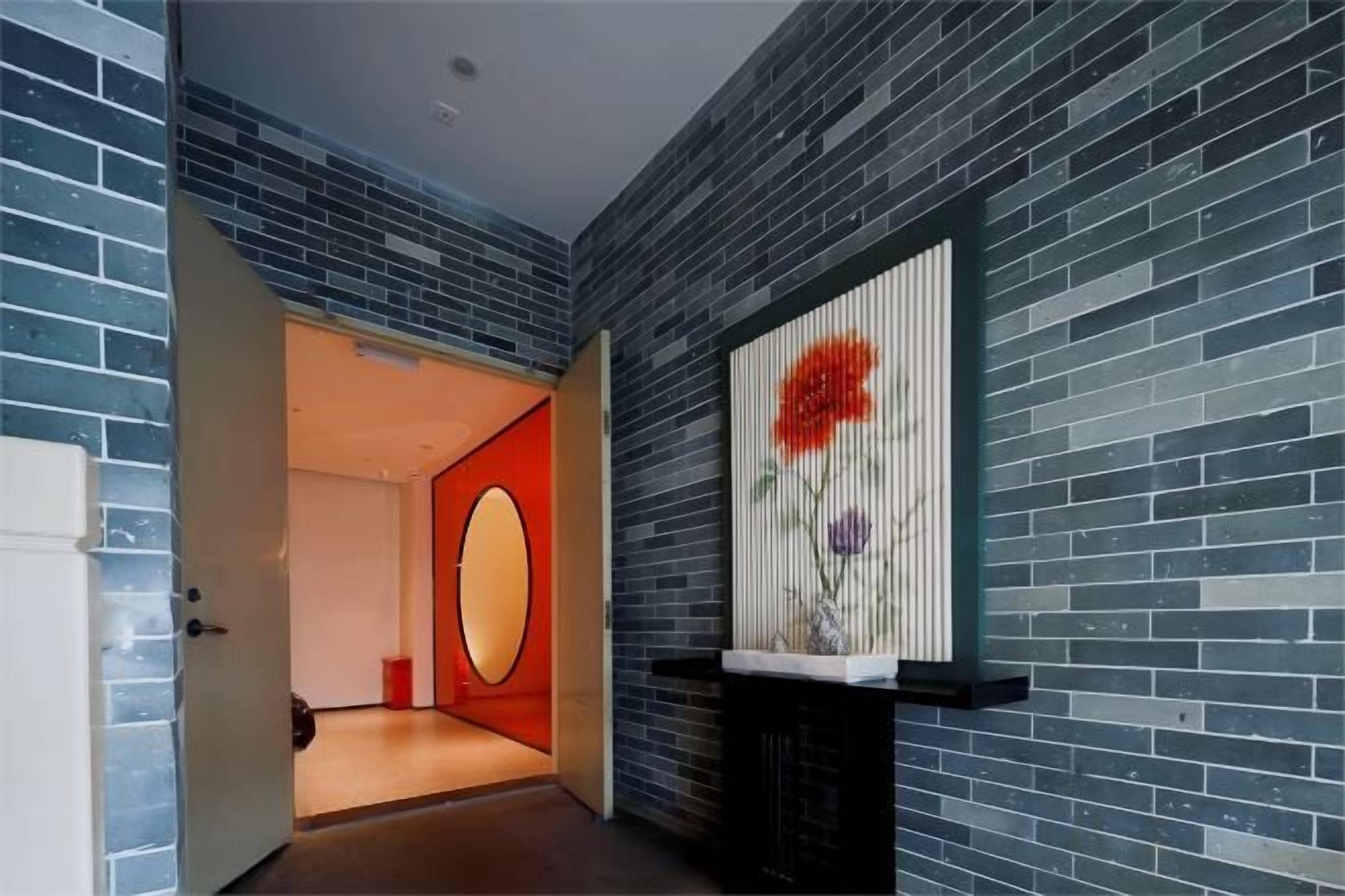 A hallway with a brick wall, a door leading to a room, and a decorative panel with a floral design.