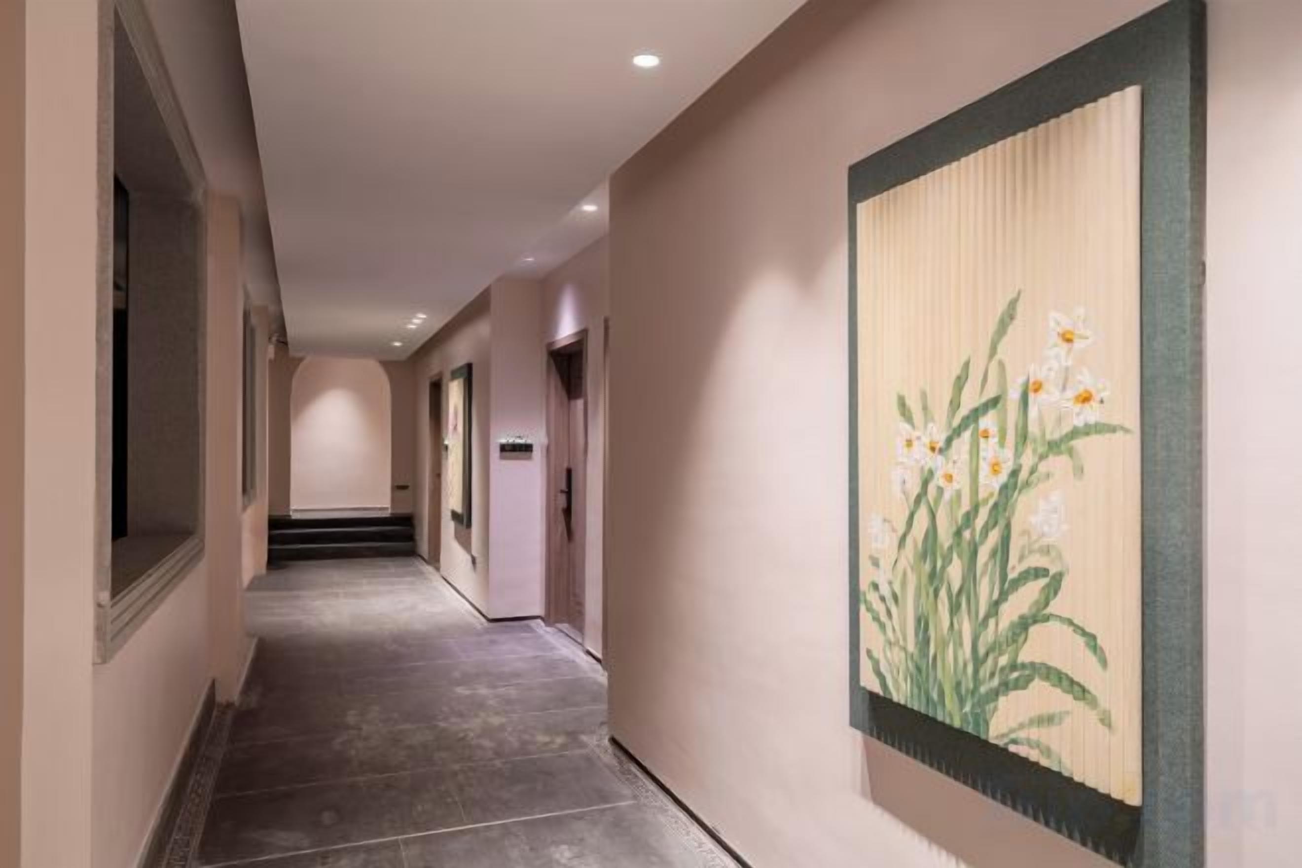 A hallway with a tiled floor, a framed artwork on the wall, and a door at the end.