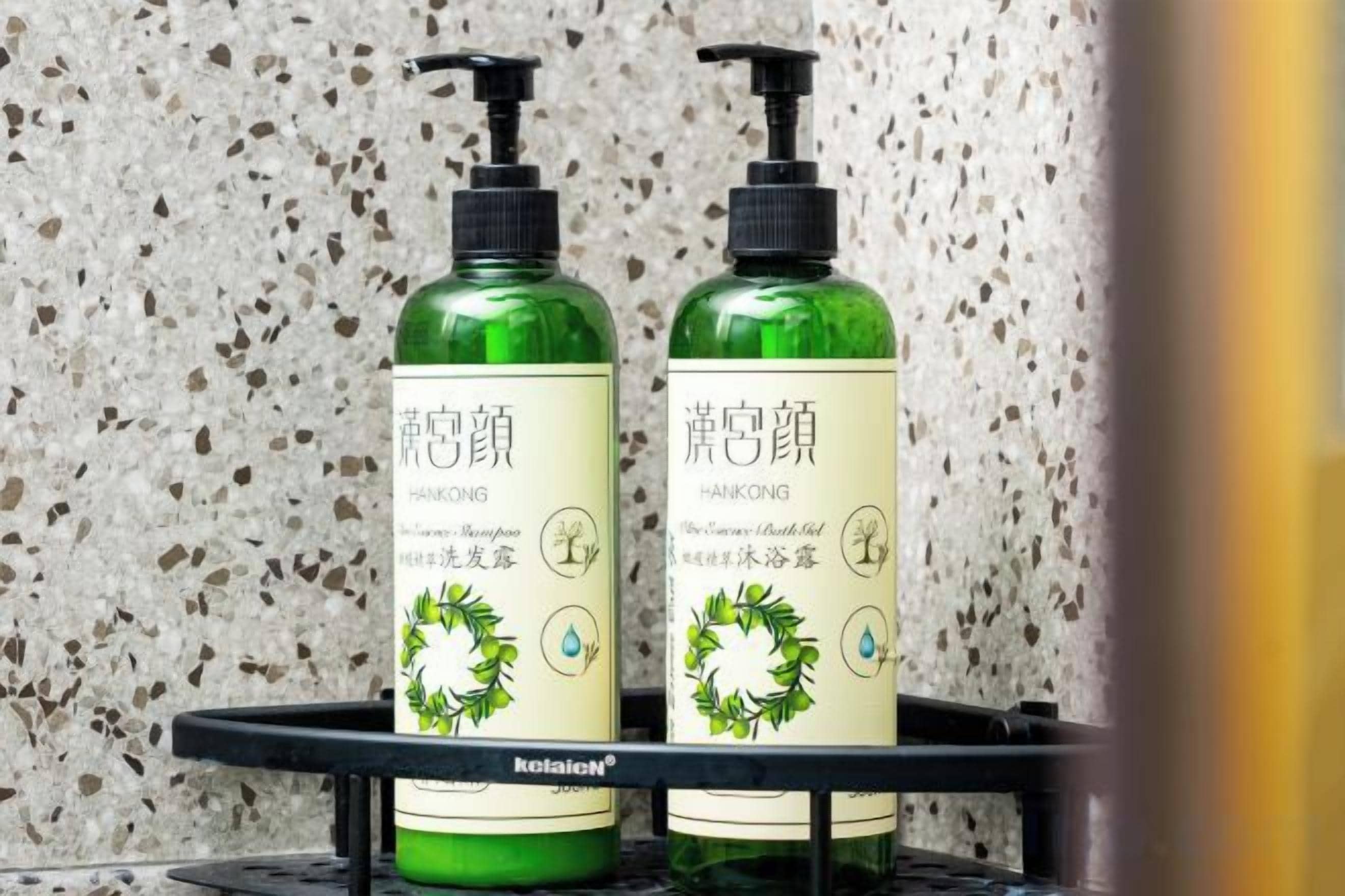 Two bottles of hair care product on a black shelf against a speckled wall.