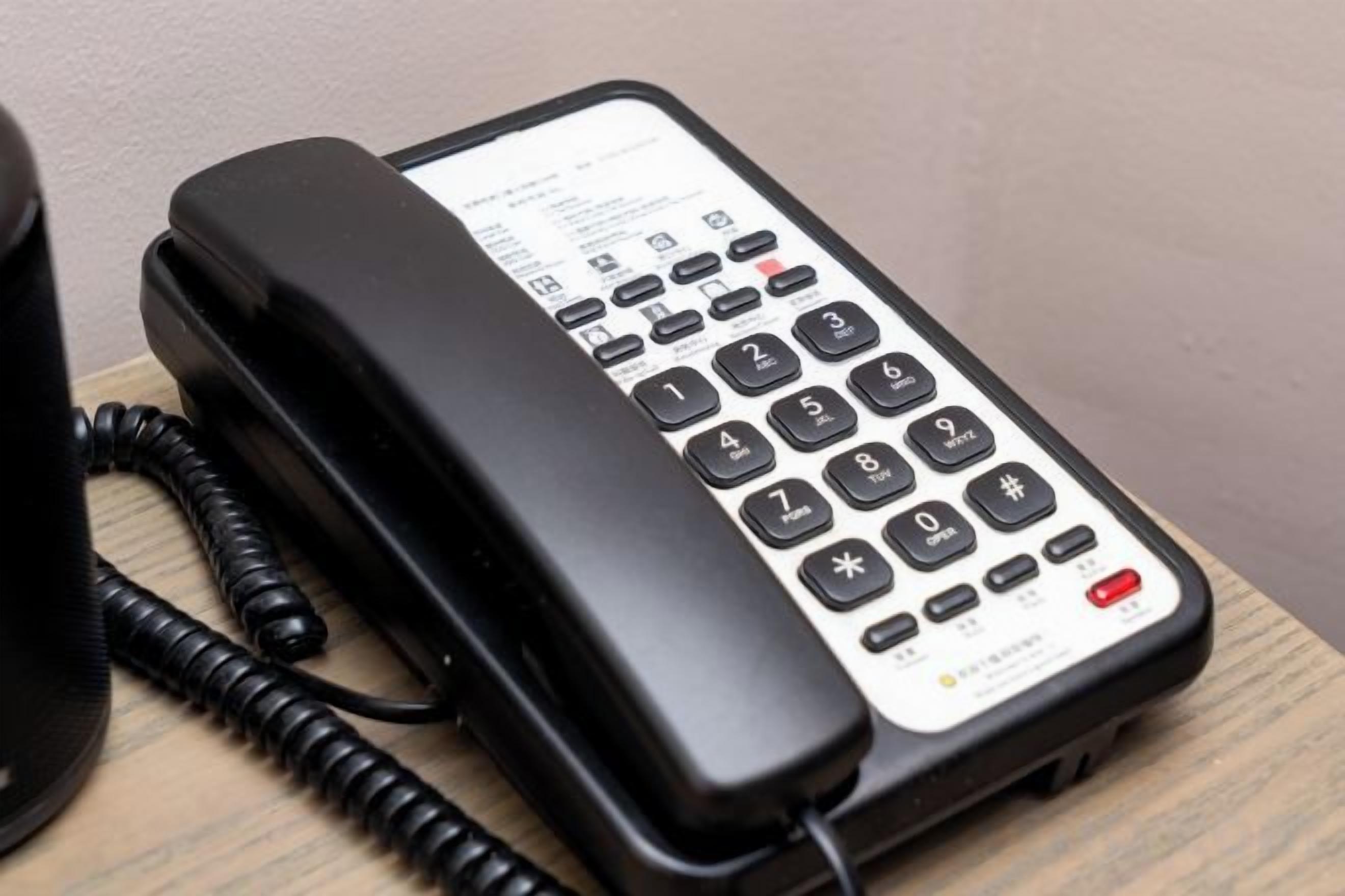 A black corded telephone with a keypad and a paper display on a wooden surface.