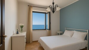 A bedroom with a bed, a nightstand, a dresser, a window with a view of the sea, and a chandelier. - Villa Lucia Sea View Holiday Home (Marina di Palma)