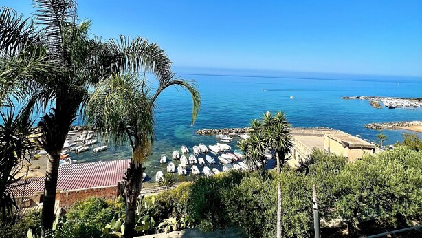 A coastal view with boats docked at a marina, palm trees, and a clear blue sky. - Villa Lucia Sea View Holiday Home (Marina di Palma)