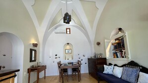 A spacious living area with a dining table, a sofa, and a bookshelf. - The Commander s House (Santorini)