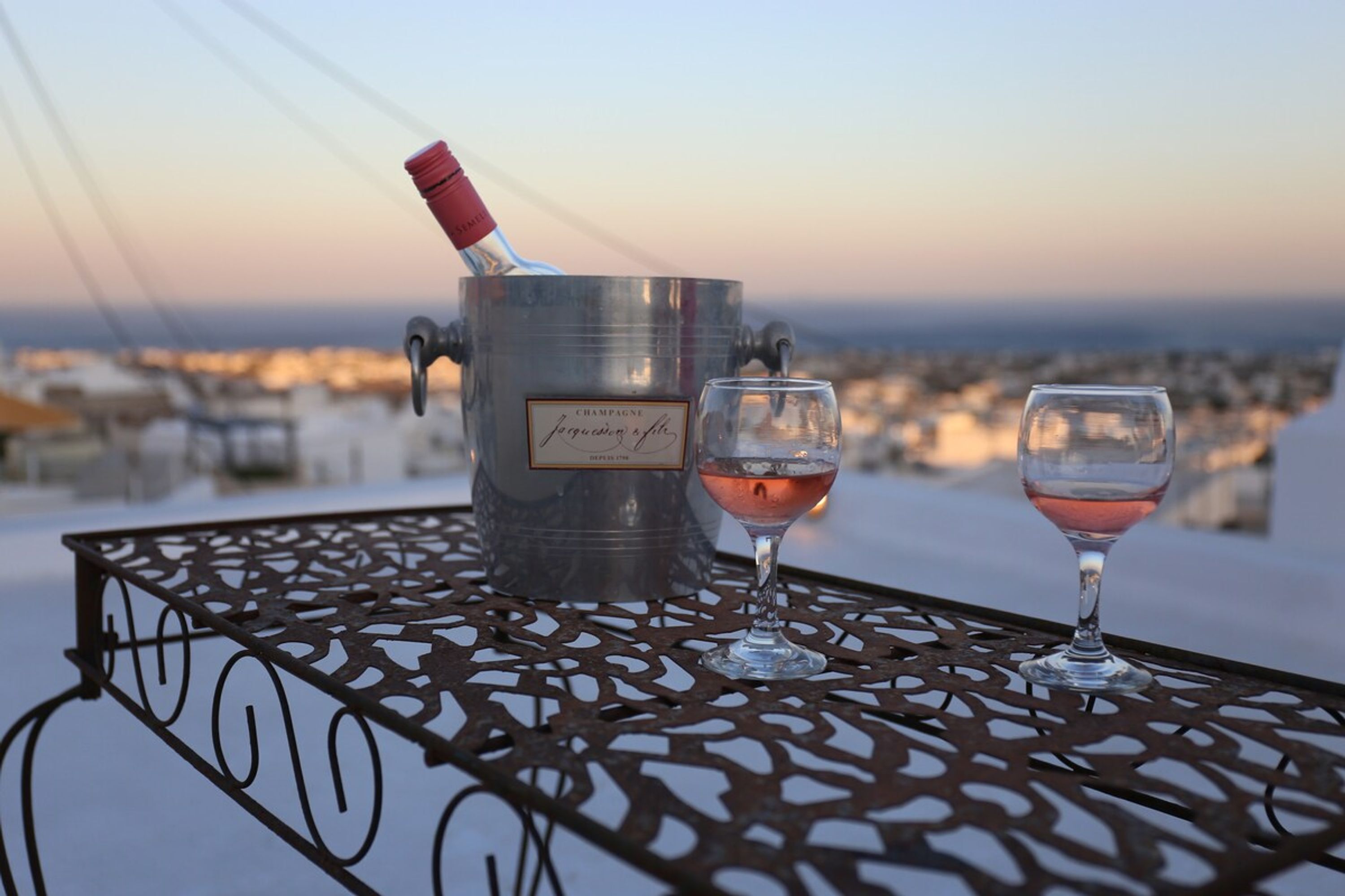 Una mesa de metal con una botella de champán y dos copas, frente a un paisaje pintoresco.